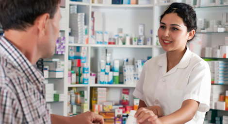 A female pharmacist smiling at a customer as she passes him some medication