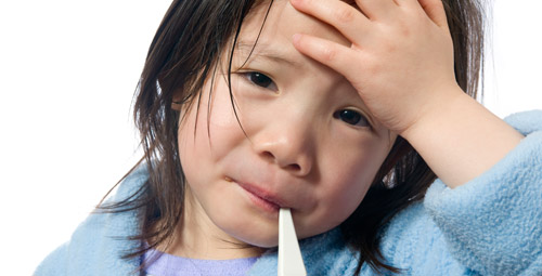 A young girl with a thermometer in her mouth and her hand held against her forehead she looks unwell