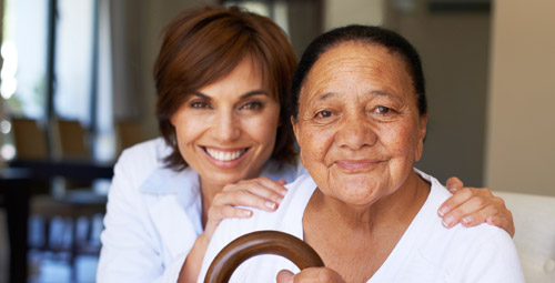 An older woman being hugged from behind by a healthcare professional